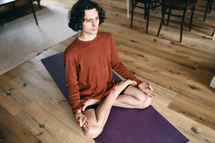 Young man sitting cross-legged on a yoga mat, appearing calm and focused, illustrating effects of anesthesia on patients.