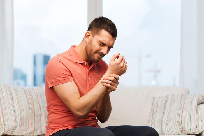 Man in red shirt on a couch holding his wrist in pain, illustrating unusual patient behavior under anesthesia effects.