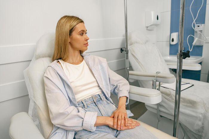Young woman sitting in a medical chair looking away, experiencing effects of anesthesia in a clinical setting.
