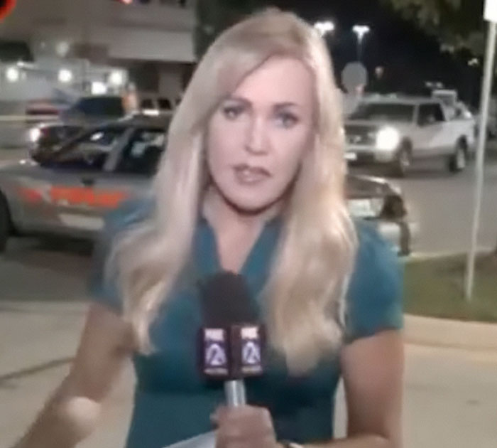 Former news anchor reporting live outdoors at night holding a microphone with police cars in the background. Former news anchor reporting live outdoors at night holding a microphone with police cars in the background.