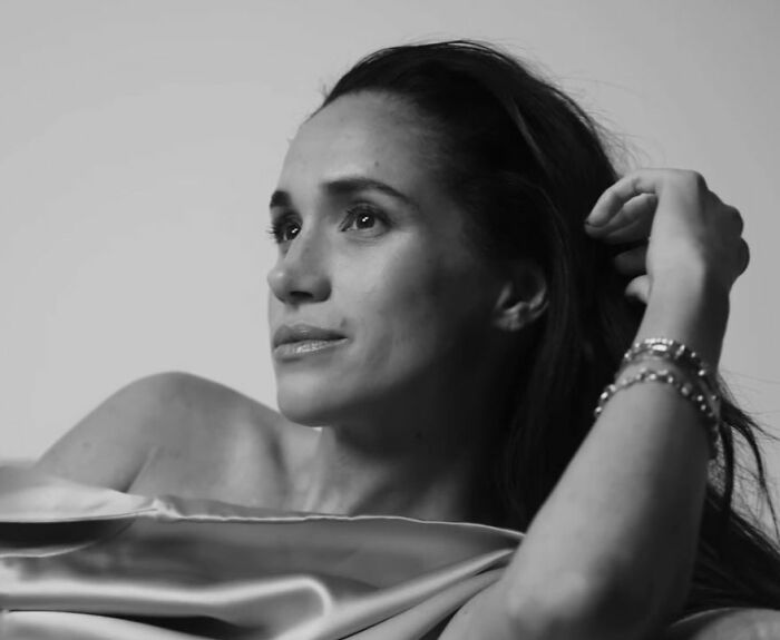 Meghan Markle in a black and white makeup-free portrait, looking contemplative and relaxed with her hand in her hair.