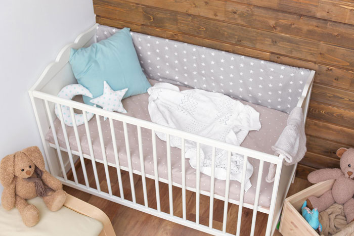 White baby crib with aunt crib storage, soft bedding, pillows, and stuffed toys in a cozy nursery corner. White baby crib with aunt crib storage, soft bedding, pillows, and stuffed toys in a cozy nursery corner.