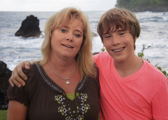 A smiling mother and teenage son posing together by the ocean, illustrating wild family dramas and relatable relatives.