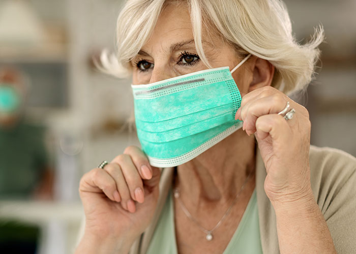 Older woman adjusting a surgical mask indoors, highlighting themes of wild family dramas and relatable family dynamics.
