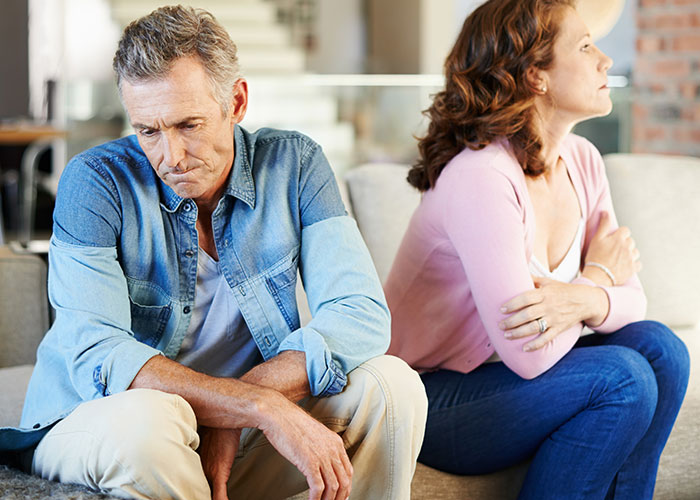 Middle-aged couple sitting apart on a couch looking upset, illustrating wild family dramas and conflict moments.