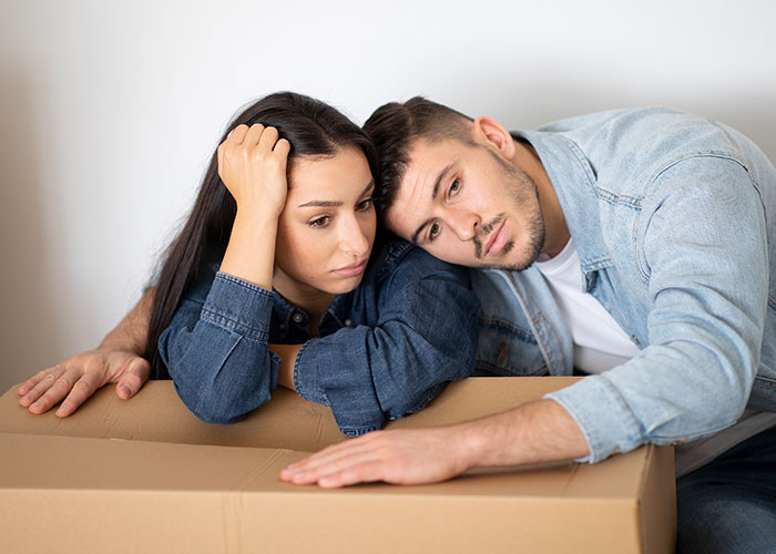 A young couple looking distressed and leaning on a cardboard box, illustrating wild family dramas and tense relationships.
