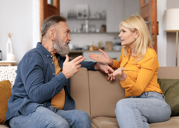Middle-aged man and woman having a wild family drama discussion on a couch, expressing frustration and emotion.