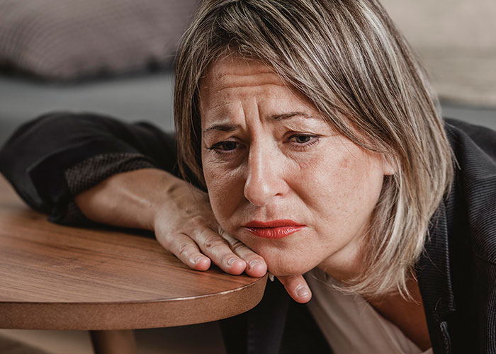 Woman with worried expression resting head on hand near wooden table, reflecting on wild family dramas and difficult relatives.