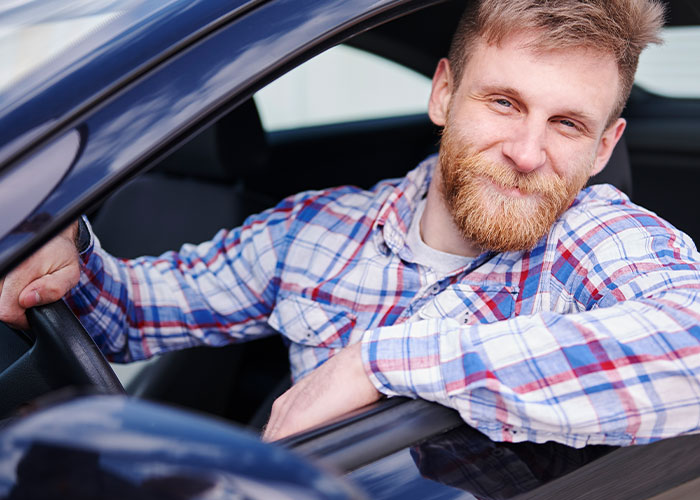 Young man with beard and plaid shirt smiling inside a car, capturing a crazy moment that wasn’t what it looked like