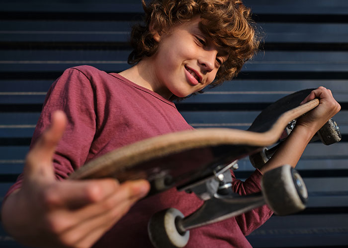 Teen boy in a red shirt examining his skateboard, capturing a crazy moment that wasn’t what it looked like.