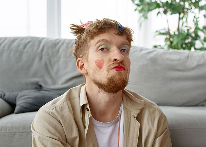 Young man with heart drawn on cheek and lipstick, making a funny face in a casual home setting showing crazy moments