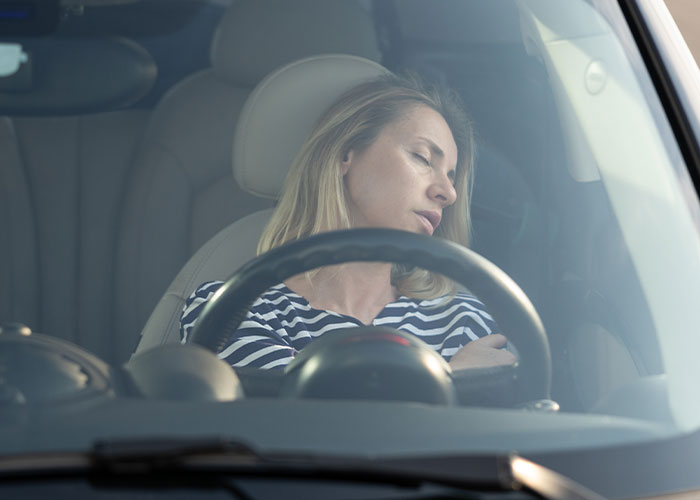 Woman asleep behind the steering wheel inside a car, illustrating crazy moments that weren’t what they looked like.