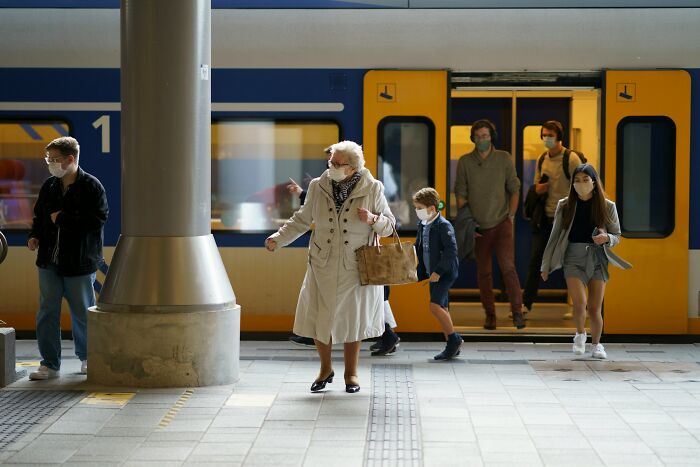Passengers wearing masks at a train station platform, representing heavy confessions and stories untold.