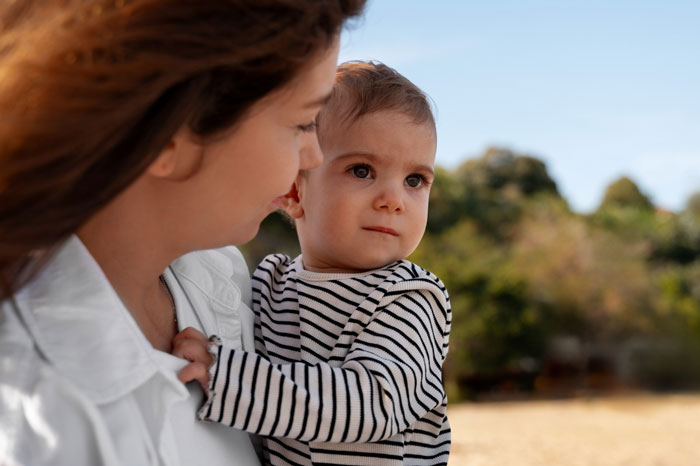 Woman at a theme park carrying an unknown baby, looking concerned as parents vanish into the crowd nearby. Woman at a theme park carrying an unknown baby, looking concerned as parents vanish into the crowd nearby.