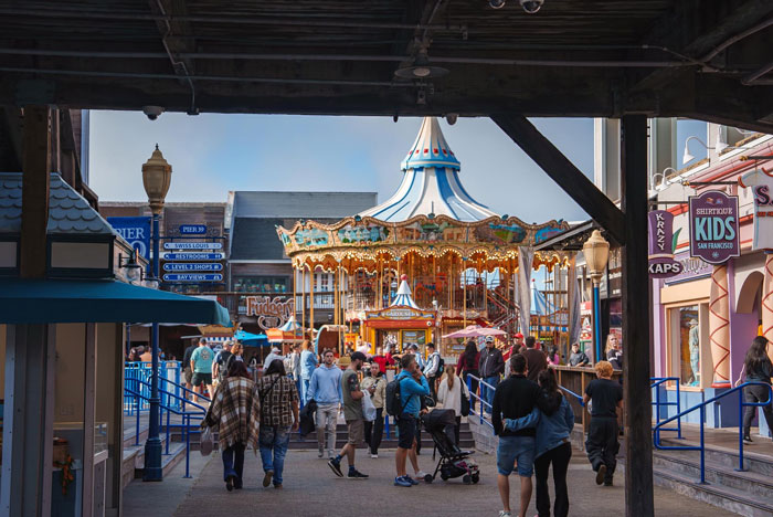 Theme park worker carrying unknown baby while parents vanish into crowd near carousel and shops on busy walkway. Theme park worker carrying unknown baby while parents vanish into crowd near carousel and shops on busy walkway.