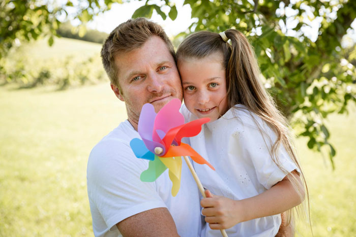 Man and child outdoors holding colorful pinwheel, representing a story about cheating and demanding babysitting from wife. Man and child outdoors holding colorful pinwheel, representing a story about cheating and demanding babysitting from wife.