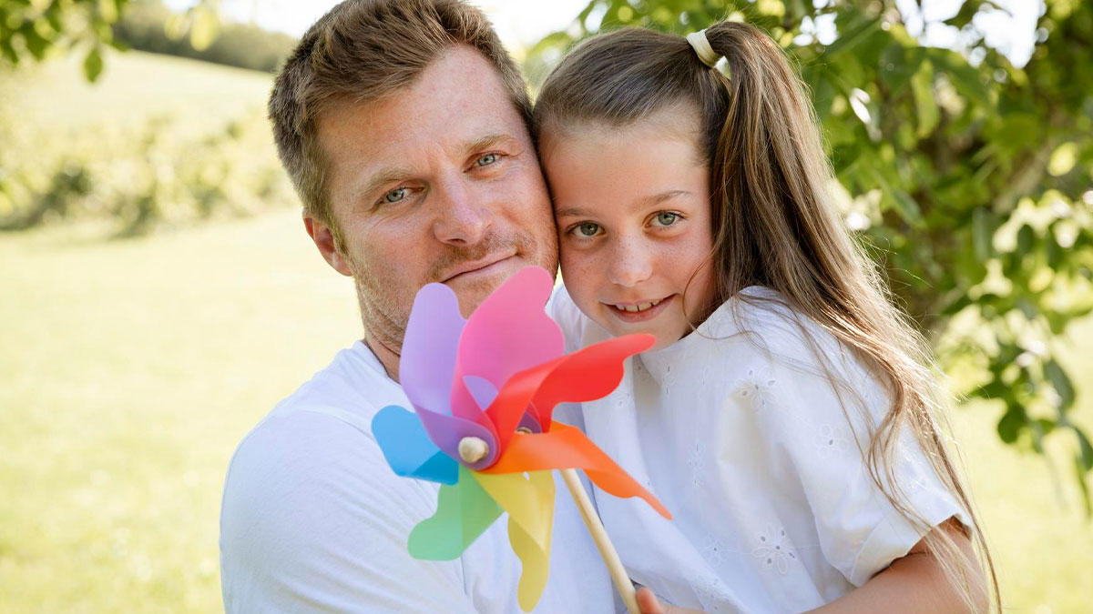 Man and daughter outdoors holding a colorful pinwheel, illustrating babysit affair child in a family setting.