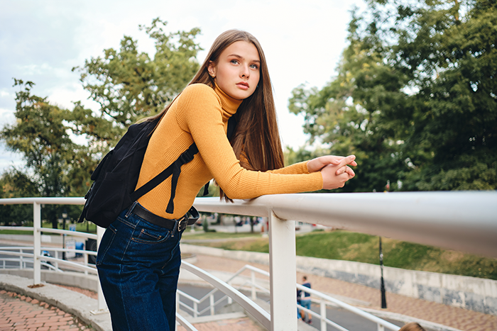 Teen girl in a yellow sweater and backpack leaning on railing, representing 17YO calling out mom retiring from parenting. Teen girl in a yellow sweater and backpack leaning on railing, representing 17YO calling out mom retiring from parenting.