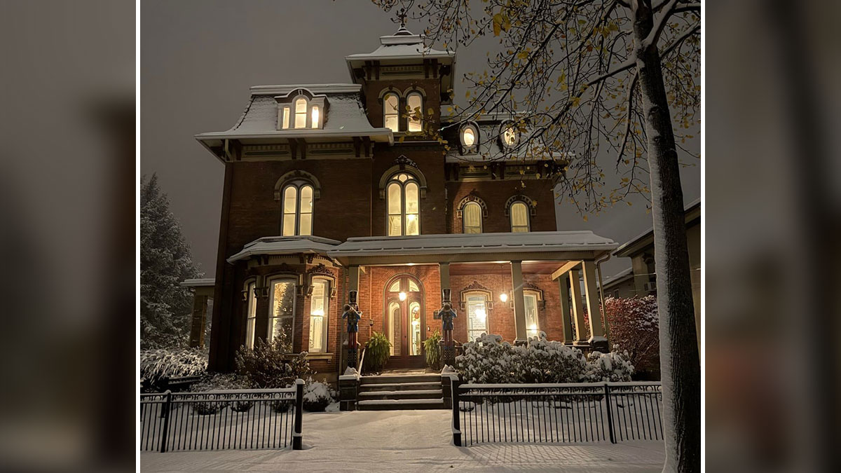 Victorian old house at night with warm lights, showcasing beautiful craftsmanship and snow-covered landscaping.