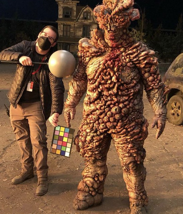 Behind-the-scenes photo of a creature costume and crew member on set showcasing unhinged moments from filming.