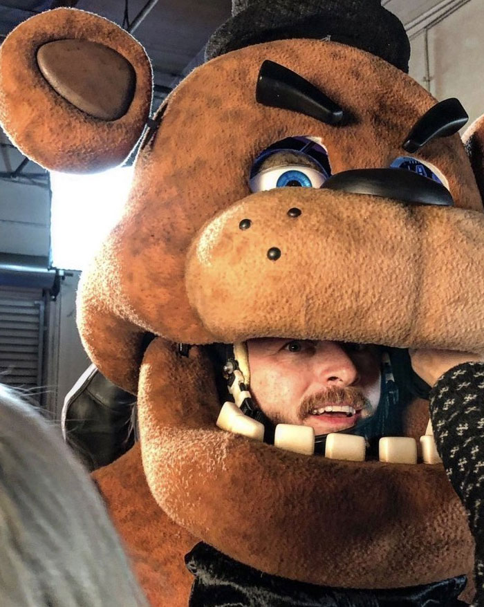 Close-up behind-the-scenes photo of a man wearing an unhinged large bear costume head, ready to become a meme.