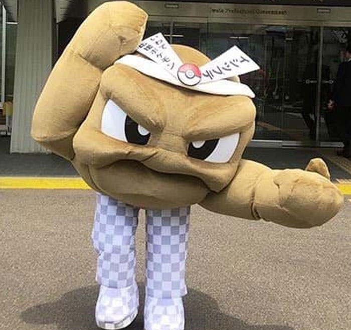 Mascot costume character posing in checkered pants with fist raised in a humorous unhinged behind-the-scenes photo.