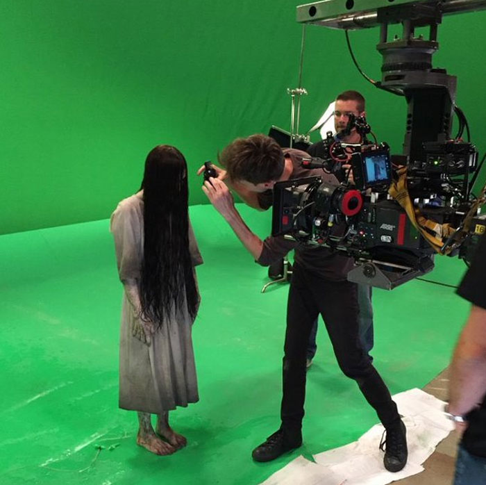 Behind-the-scenes photo of a camera crew filming a person in a creepy costume on a green screen set for meme potential.