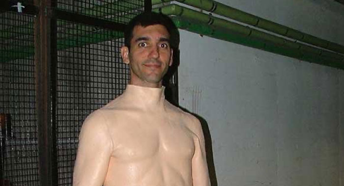 Man wearing a skin-colored bodysuit posing with a surprised expression in an unhinged behind-the-scenes photo.