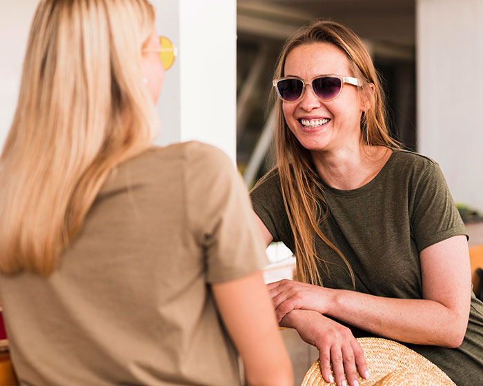 Two women smiling and chatting while sitting together, depicting a best friend no contact returns moment. Two women smiling and chatting while sitting together, depicting a best friend no contact returns moment.