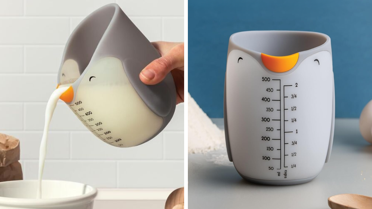 Silicone penguin-shaped kitchen measuring cup with volume markings, pouring milk into a bowl on a kitchen counter.