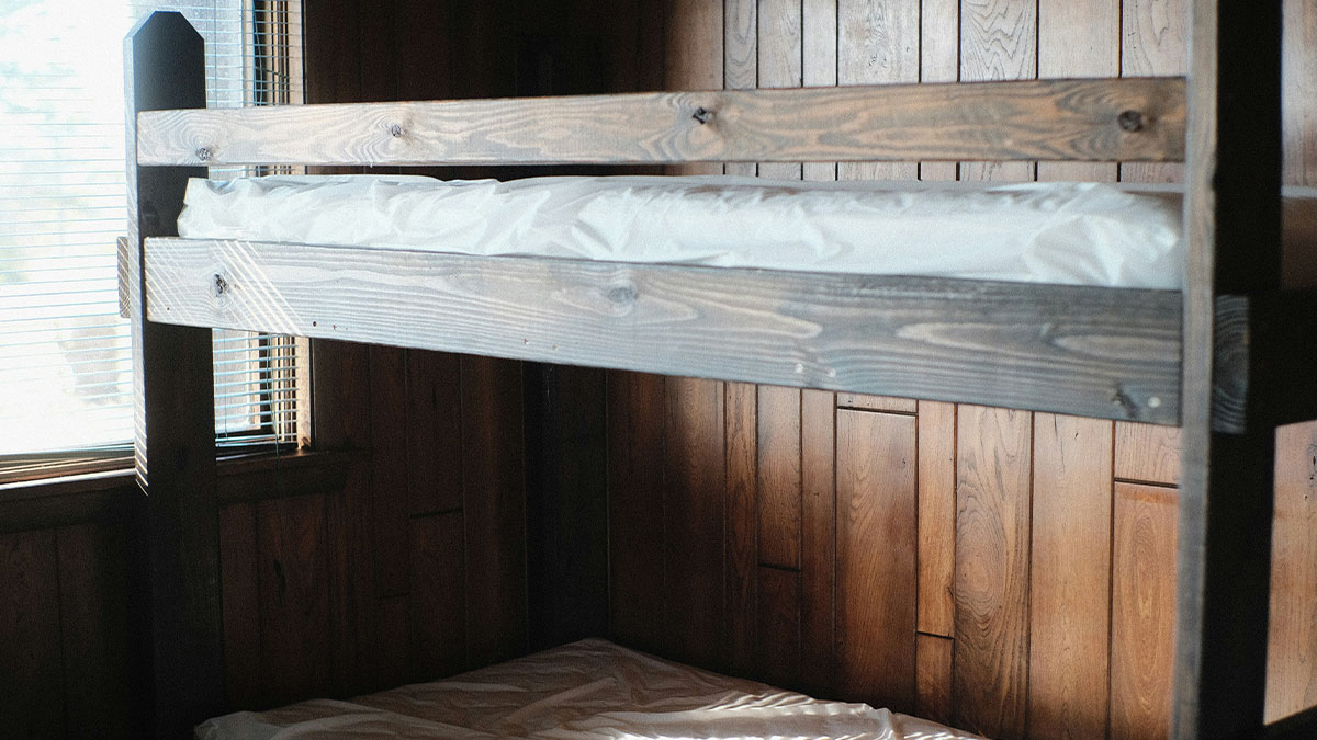 Wooden bunk beds inside a cabin room with natural light coming through blinds on the window.