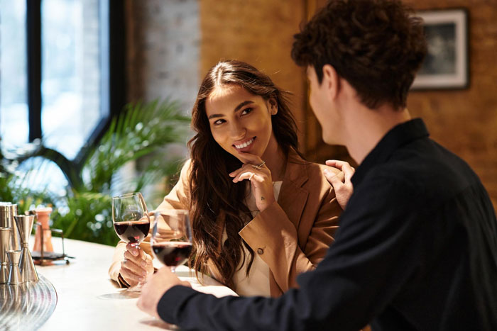 Polyamorous woman flirting with a taken guy at a bar while holding a glass of red wine in a cozy setting. Polyamorous woman flirting with a taken guy at a bar while holding a glass of red wine in a cozy setting.