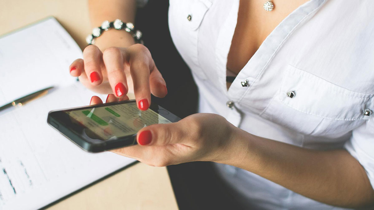 Woman with red nails in family chat on phone discussing birthday money plans while sitting at desk with notes.