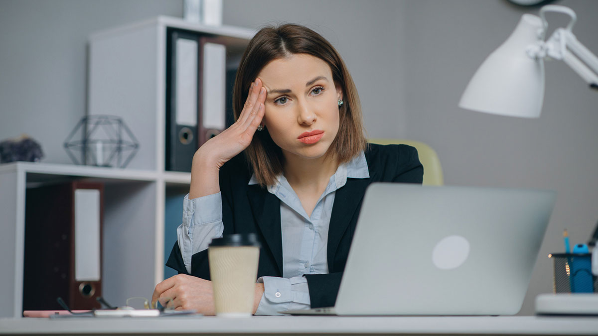Female software developer looking gobsmacked and frustrated working on laptop in an office setting with coffee cup nearby.