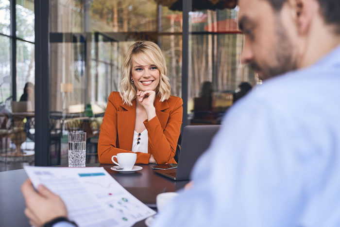 Female software developer in a client meeting looking surprised while a man reviews documents in a modern office.
