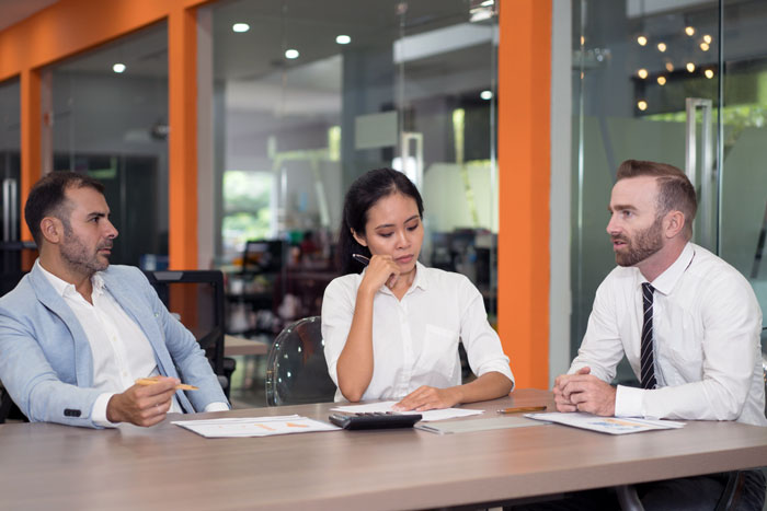 Female software developer looking thoughtful during a client meeting with two male colleagues in a modern office setting.