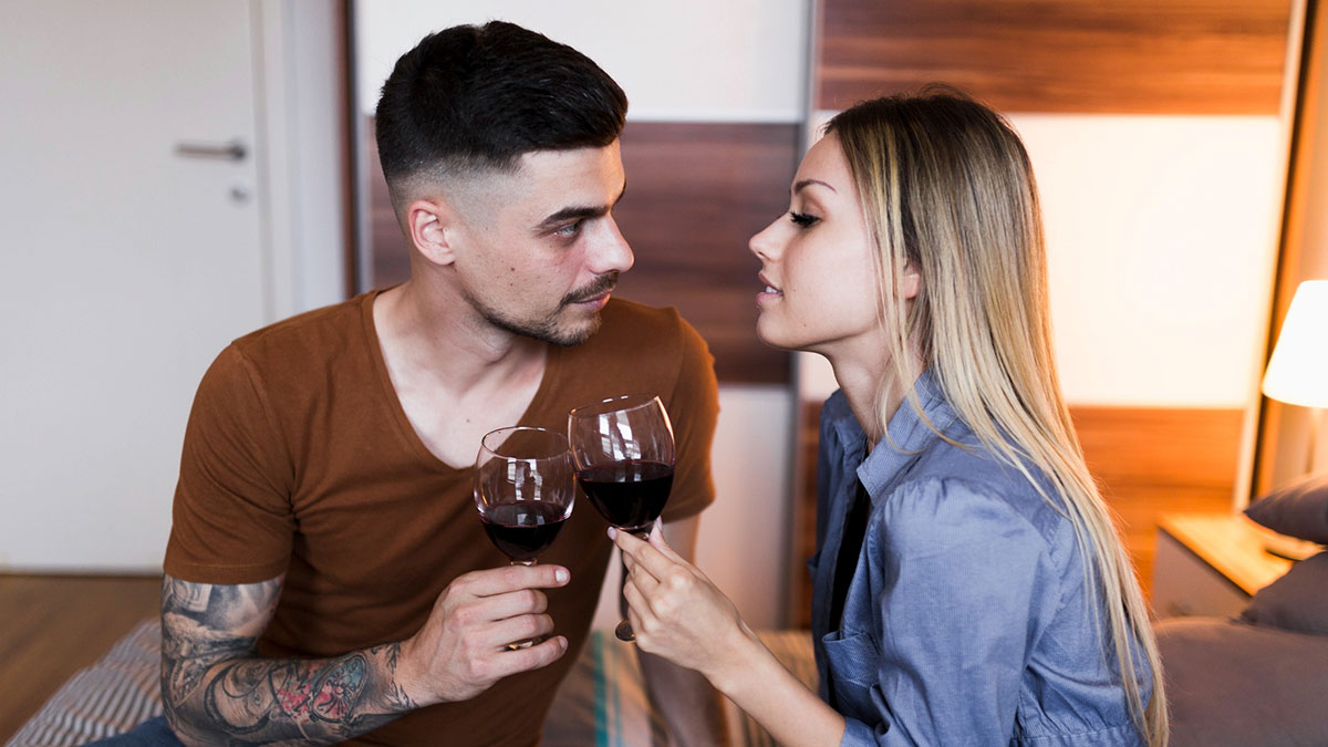 Young couple sharing wine on vacation, boyfriend and woman in intimate moment indoors with serious expressions