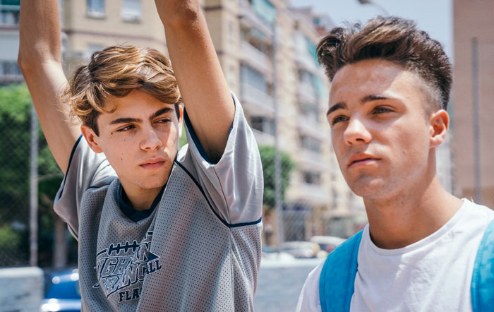 Two young men outdoors, one raising his arms, highlighting sibling rivalry and relationship tension. Two young men outdoors, one raising his arms, highlighting sibling rivalry and relationship tension.