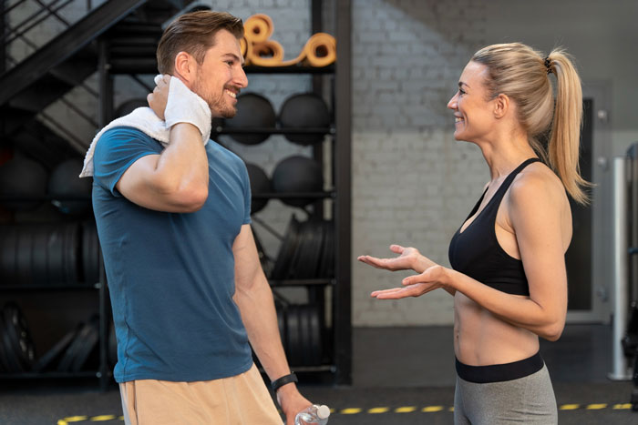 A man laughing while talking to a woman at the gym, depicting a sibling rivalry trophy relationship moment. A man laughing while talking to a woman at the gym, depicting a sibling rivalry trophy relationship moment.