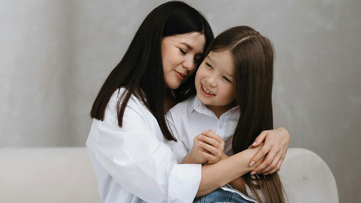 Mother and daughter sharing a close moment, smiling and embracing each other gently in a calm indoor setting.
