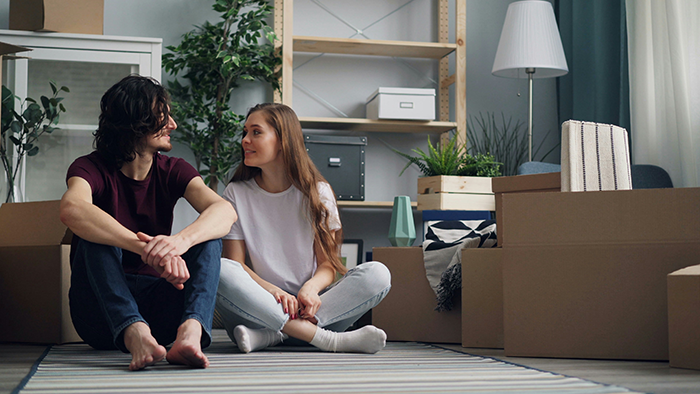 Young couple sitting on the floor among moving boxes, discussing a $100k renovation and relationship finances. Young couple sitting on the floor among moving boxes, discussing a $100k renovation and relationship finances.