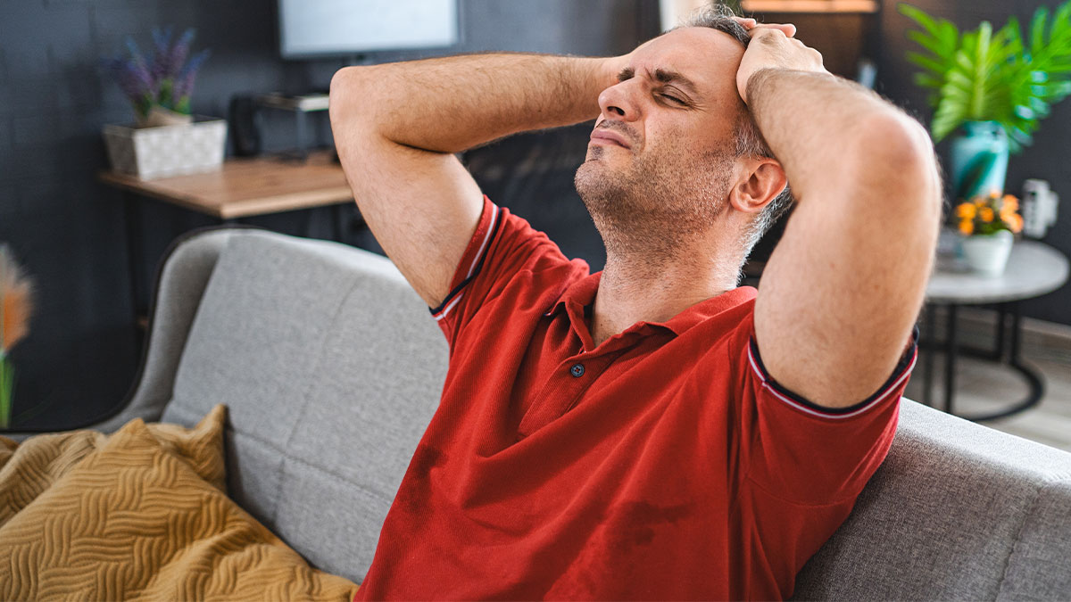 Man in a red shirt sitting on a couch looking stressed and frustrated, relating to boyfriend opens relationship gets no dates.