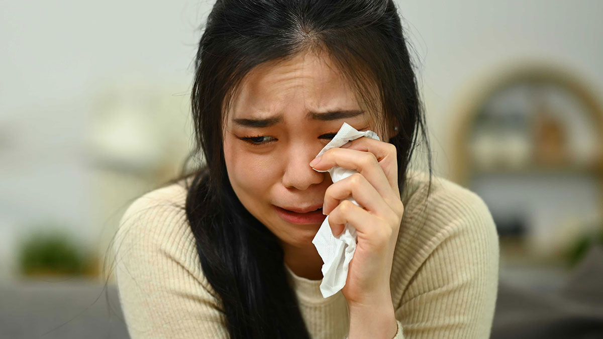 Woman wiping tears, emotionally upset, reflecting on leaving the US to start a new life in France after success challenges.