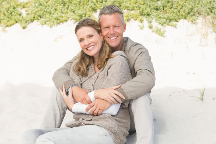 Couple sitting on the sand, smiling and embracing, illustrating GF feels uneasy every time BF mentions moving in concerns. Couple sitting on the sand, smiling and embracing, illustrating GF feels uneasy every time BF mentions moving in concerns.