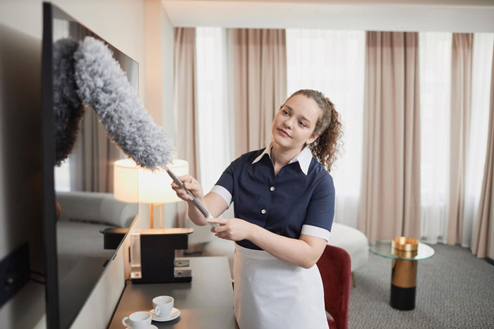 Woman feeling uneasy dusting TV in hotel room, reflecting GF feels uneasy every time BF mentions moving in. Woman feeling uneasy dusting TV in hotel room, reflecting GF feels uneasy every time BF mentions moving in.