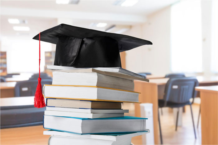 Graduation cap placed on a stack of books in a bright, empty university classroom symbolizing education and university life.