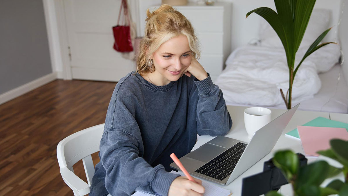 Young woman studying online at home with laptop and notebook, representing 20-year-old university student concept.