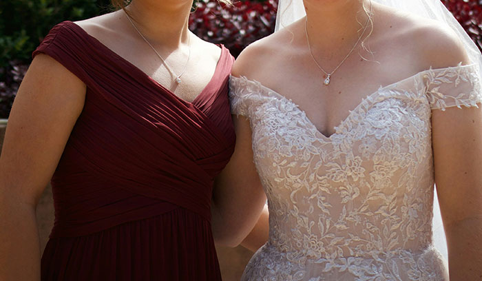 Bride in lace wedding dress standing next to cousin in a dark red dress, outdoors with natural light. Bride in lace wedding dress standing next to cousin in a dark red dress, outdoors with natural light.