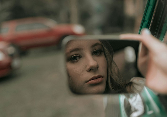Close-up of a woman’s face reflected in a car mirror, capturing a bride mad at cousin over dress at wedding. Close-up of a woman’s face reflected in a car mirror, capturing a bride mad at cousin over dress at wedding.