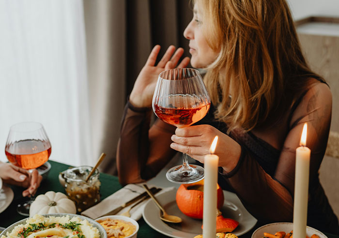 Woman holding a glass of wine at a dinner table, appearing upset, relating to bride mad cousin dress wedding emotions.